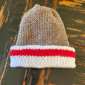 May include: A brown knit beanie with a white and red stripe around the bottom.