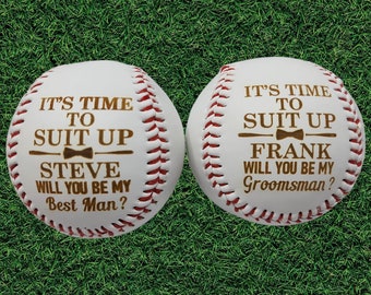 May include: Two white baseballs with red stitching. One baseball has the text "IT'S TIME TO SUIT UP STEVE WILL YOU BE MY BEST MAN?" The other baseball has the text "IT'S TIME TO SUIT UP FRANK WILL YOU BE MY GROOMSMAN?"