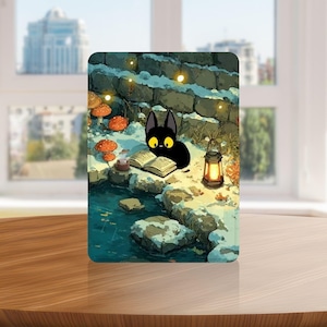 以下が含まれることがあります： 小川のそばで本を読む、黄色の目をした黒猫が描かれた長方形のアートプリント。シーンにはキノコ、ランタン、石壁が含まれており、雪に覆われた気まぐれな雰囲気です。プリントは木製の表面に表示されています。