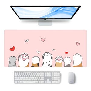 Könnte beinhalten: Ein rosa rechteckiges Schreibtisch-Pad mit einem sich wiederholenden Muster aus Cartoon-Katzenpfoten und Herzen. Eine Computertastatur, eine Maus und ein Monitor sind ebenfalls sichtbar. Das Schreibtisch-Pad ist für die Verwendung mit einem Computer konzipiert.