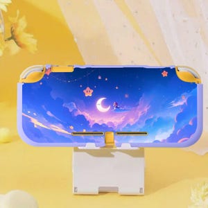 May include: A purple and yellow Nintendo Switch Lite case featuring a dreamy night sky design with a crescent moon, stars, and clouds. The case is resting on a white stand, showcasing the colorful artwork. The case is designed to protect the console.