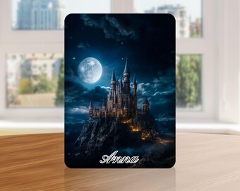 May include: A rectangular plaque featuring a nighttime castle scene under a full moon. The castle is perched on a rocky cliff, with the name "Anna" in cursive at the bottom. The color palette includes blues, blacks, and golds.