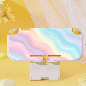 Op de afbeelding: Een Nintendo Switch Lite-console in pastelkleuren met een regenbooggolfontwerp. Het draagbare spelapparaat heeft gele accenten. De console staat op een witte standaard tegen een gele achtergrond. Afmetingen: ongeveer 21 cm breed.