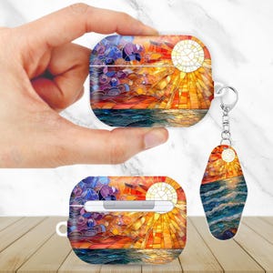 May include: AirPod case and keychain with a stained-glass sunset design. The case is square with a curved top, and the keychain is teardrop-shaped. The design features orange, yellow, blue, and purple hues, reminiscent of a seascape.