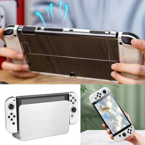 May include: A white Nintendo Switch console with a clear protective case. The console is in a tabletop mode with the screen facing forward. The console is on a white surface.