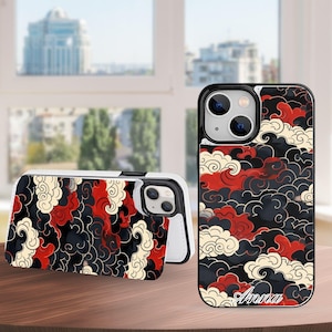 Peut inclure: Coque de téléphone noire, rouge et crème avec un motif de nuages. L'étui est présenté ouvert et fermé. Le nom "Anna" est imprimé en blanc sur le devant de l'étui.