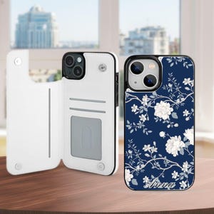 May include: A white wallet-style phone case with interior card slots and a magnetic closure, paired with a matching dark blue phone case featuring a white floral pattern and the name Anna printed in white script at the bottom of the case.