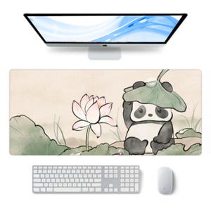 May include: A rectangular desk mat with a panda bear under a leaf, a lotus flower, and leaves. The mat has a light beige background. A white keyboard and mouse are below. The mat's dimensions are approximately 70 cm x 30 cm.