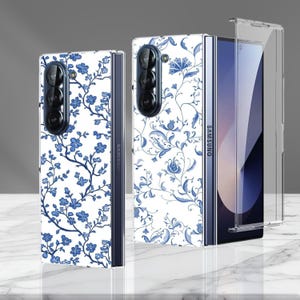 Puede incluir: Fundas para teléfonos plegables Samsung con un patrón floral blanco y azul. Las fundas muestran un diseño floral azul detallado sobre un fondo blanco. El teléfono está parcialmente abierto, mostrando la pantalla y el logotipo de Samsung.