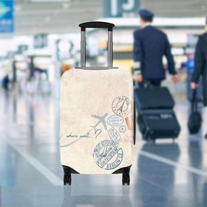 Peut inclure: Une valise à roulettes crème avec un thème de voyage. La valise présente un design avec des timbres, un avion et la phrase "where next...?" en écriture manuscrite. Elle a une poignée rétractable et des roues noires.