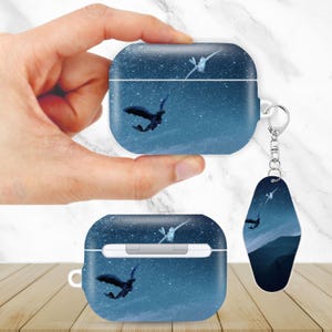 May include: AirPod case and keychain featuring a night sky design with a dragon and a white bird in flight. The case is a square shape with a white interior. The keychain has a silver ring.