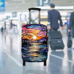 May include: A rolling suitcase with a colourful stained-glass design featuring a sunset over a lake. The design includes shades of orange, yellow, blue, and purple. The suitcase has a black handle and wheels.
