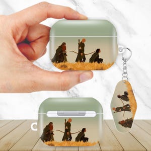 May include: Green and white AirPod case and keychain featuring a landscape scene with three figures in cloaks and a fourth figure kneeling in a field of tall grass. The keychain has the same design.