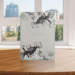 Op de afbeelding: Een witte en grijze tablet hoes met een drakenontwerp en de naam "Anna". De hoes heeft een citaat: "Voor degenen die zich klein en stil voelen. Spreid je vleugels en brul."