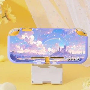 Può includere: Una custodia lilla e gialla per Nintendo Switch Lite con un design a paesaggio fantasy, tra cui un castello, un arcobaleno e nuvole. Il nome "Anna" è scritto in corsivo. La custodia è su un supporto bianco.
