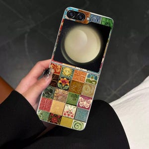 Puede incluir: Una funda de teléfono colorida con un diseño de mosaico. La funda presenta un diseño circular grande en la mitad superior y un mosaico de pequeños azulejos cuadrados con varios diseños en la mitad inferior. La funda se sostiene en una mano.