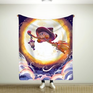 May include: A large, rectangular blanket featuring a cartoon character riding a broom in front of a full moon. The character wears a cowboy hat and holds a lantern. The background includes clouds and stars, with a color palette of purple, orange, and yellow.