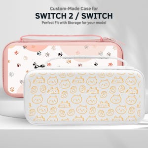 May include: Two custom-made cases for SWITCH 2 / SWITCH. The front case is white with a pattern of orange cat faces and paws. The back case is pink with a pattern of paw prints. Both cases have a zipper closure and a handle.