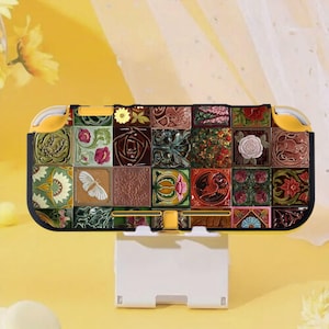 Op de afbeelding: Een decoratieve Nintendo Switch Lite-hoes met een mozaïekontwerp van bloemen- en geometrische patronen in verschillende kleuren. De hoes heeft gele accenten en staat op een witte oplaadstandaard. De mozaïek bevat een vlinder en een vogel.