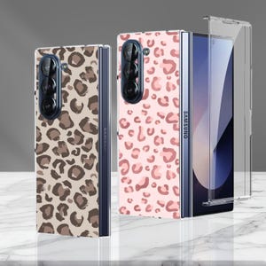 Könnte beinhalten: Zwei Samsung Galaxy Z Fold Handyhüllen. Eine Hülle hat einen braunen und beigen Leopardenmuster, die andere ein rosa Leopardenmuster. Eine transparente Schutzhülle ist ebenfalls abgebildet. Die Telefone haben eine Dreifach-Kamera.