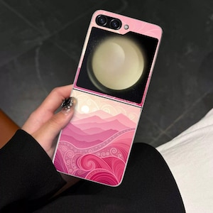 May include: A pink smartphone case with a landscape design featuring layered pink mountains and swirling patterns. The phone's screen displays a bright, circular image. The case has a dual-camera setup.