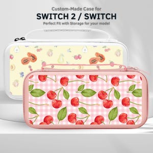 Può includere: Due custodie personalizzate per Switch 2 / Switch. Una è bianca con un motivo di frutta gialla, l'altra è rosa con un motivo di ciliegie. Le custodie hanno una chiusura a zip e un manico.