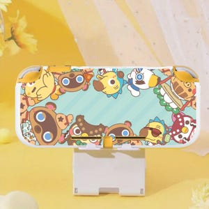 Può includere: Una console Nintendo Switch Lite bianca e gialla con un design di personaggi dei cartoni animati. La custodia presenta vari personaggi di animali su uno sfondo azzurro con dettagli gialli. La console è su un supporto bianco.