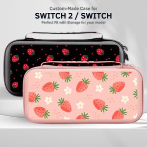 Peut inclure: Deux étuis personnalisés pour SWITCH 2 / SWITCH. L'un est noir avec un motif de fraises, l'autre est rose avec des fraises et des fleurs blanches. Les deux étuis ont une fermeture éclair et une poignée.
