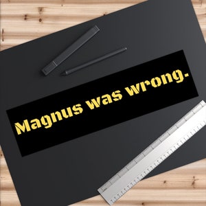 Puede incluir: Pegatina negra y amarilla con el texto "Magnus estaba equivocado." sobre una superficie negra.