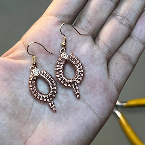 Peut inclure: Une paire de boucles d'oreilles en fil de rose gold en forme de larme avec un détail en spirale en haut.