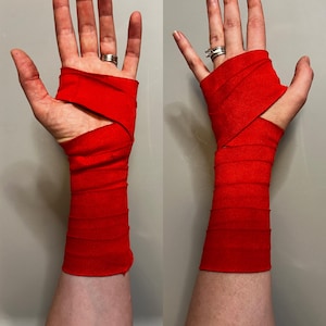 Op de afbeelding: Twee handen met rode bokswraps. De wraps bedekken de polsen en een deel van de handen, met een open gedeelte voor de handpalm. De wraps zijn effen, levendig rood.