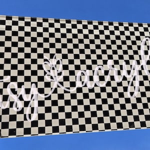 May include: A black and white checkered pattern on a clear acrylic sheet. The sheet is held in a hand and the text "artsy acrylic" is written across the sheet.