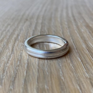 May include: A silver ring with a smooth, rounded surface and a subtle groove around the center.
