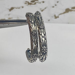 May include: A pair of silver hoop earrings with a floral design. The earrings are made of metal and have a shiny finish.