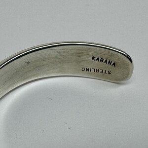 May include: A curved, silver-toned bracelet. The inside of the bracelet is stamped with the word "KABANA" above "STERLING". The bracelet has a smooth, polished finish and is set against a light background.