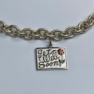 Może przedstawiać: Srebrna bransoletka z zawieszką z napisem "Get Well Soon" i czerwono-zielonym kwiatem.