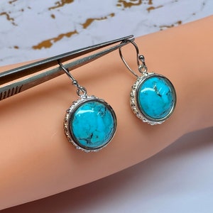 Könnte beinhalten: Ein Paar silberne Ohrhänger mit türkisfarbenen Steinen, die in einer runden Fassung sitzen. Die Steine haben ein marmoriertes Muster und sind hellblau.