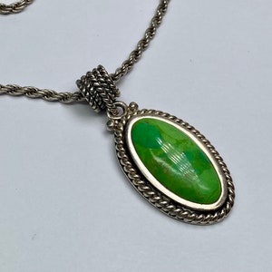 Pode incluir: Um colar de corrente de prata com um pingente de turquesa oval verde. O pingente tem uma borda de corda.