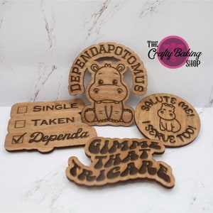 May include: Five wooden laser-cut signs with a hippopotamus theme. The signs read "Dependapotamus", "Gimme That Tricare", "Single", "Taken", and "Salute Me! I Serve Too!"