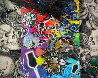 May include: A colorful, artistic composition featuring a book titled "Lunaria's Oracle" with a rainbow background. Adornments include charms, crystals, and a decorative spoon. The background has a skull and rose pattern.