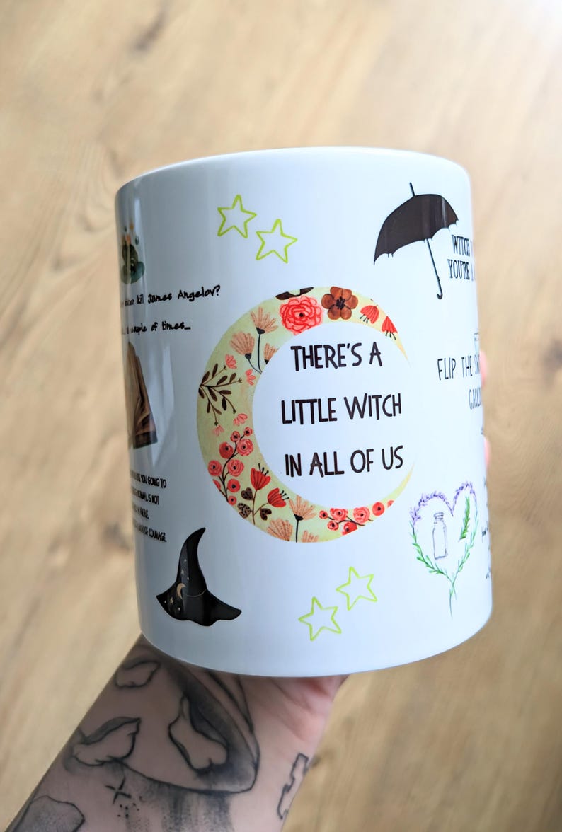 Puede incluir: Una taza de cer&aacute;mica blanca con un gr&aacute;fico de luna creciente lleno de patrones florales y el texto "THERE'S A LITTLE WITCH IN ALL OF US". Las ilustraciones adicionales incluyen un sombrero de bruja negro, un paraguas, estrellas y citas.