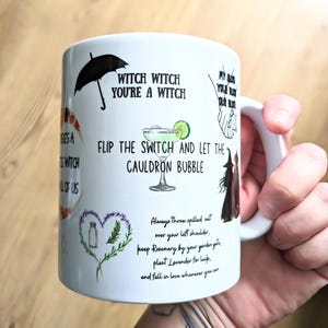 Puede incluir: Una taza de cer&aacute;mica blanca con varios textos en negro e ilustraciones coloridas, incluyendo un paraguas negro, una copa de margarita, un coraz&oacute;n hecho de lavanda y romero, y las frases Witch Witch You're A Witch y Flip The Switch And Let The Cauldron Bubble.