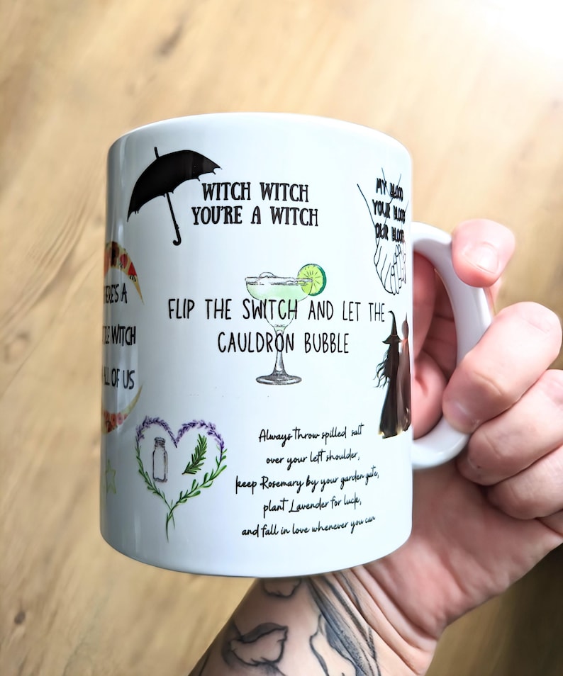 Puede incluir: Una taza de cer&aacute;mica blanca con varios textos en negro e ilustraciones coloridas, incluyendo un paraguas negro, una copa de margarita, un coraz&oacute;n hecho de lavanda y romero, y las frases Witch Witch You're A Witch y Flip The Switch And Let The Cauldron Bubble.