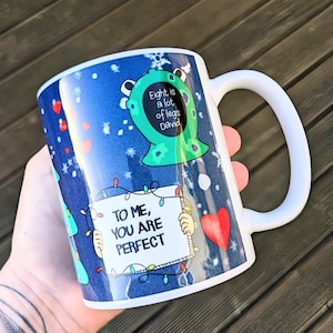 May include: White ceramic mug with a blue background, decorated with a green monster, snowflakes, and hearts. The mug has the text "Eight is a lot of legs David" and "To me, you are perfect."