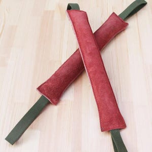 May include: Two red leather dog chew toys with green straps. The toys are crossed over each other.