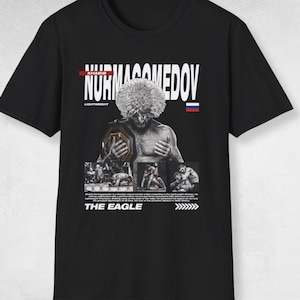 Puede incluir: Camiseta negra con un gráfico de un artista marcial mixto sosteniendo un cinturón de campeonato. La camiseta incluye el nombre "NURMAGOMEDOV" en texto blanco, la bandera rusa y las palabras "THE EAGLE".