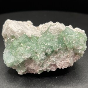May include: A cluster of green crystals embedded in a white matrix. The crystals are translucent and have a glassy lustre. The matrix is rough and textured.