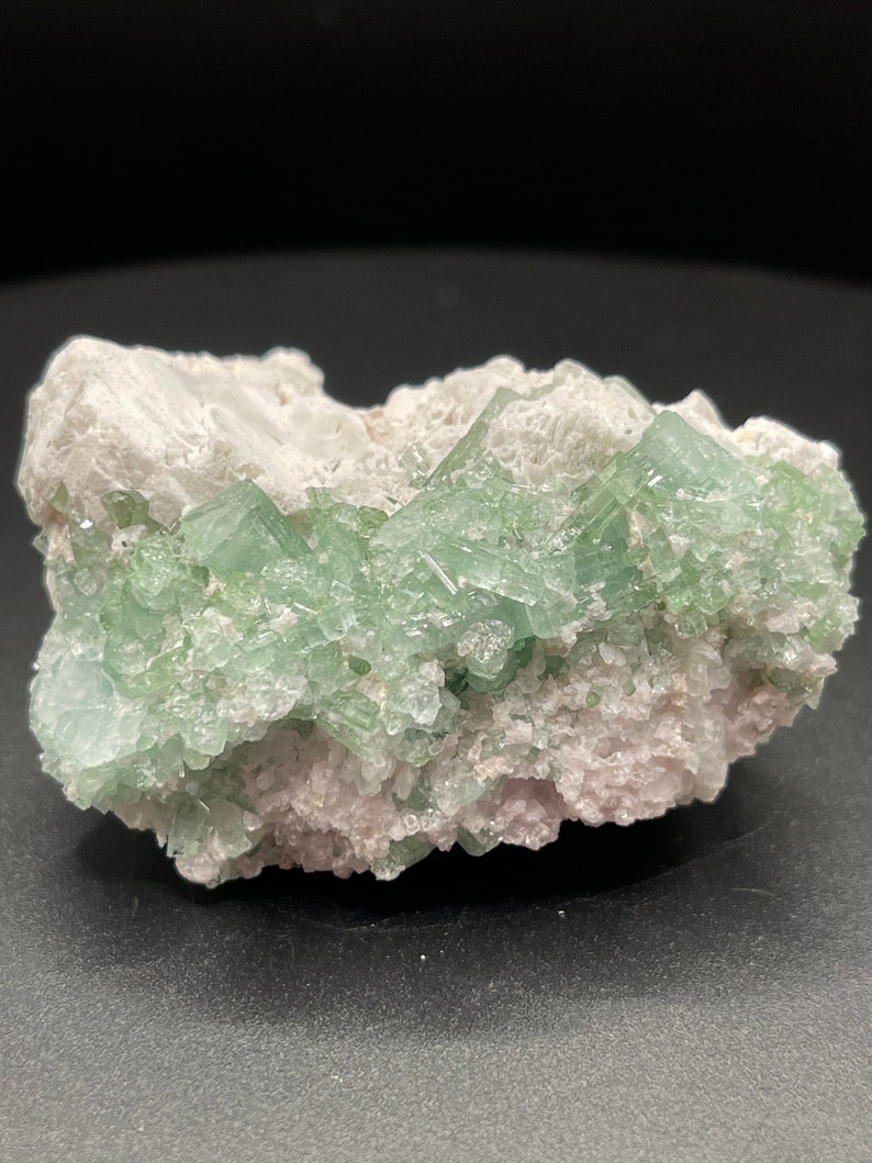 May include: A cluster of green crystals embedded in a white matrix. The crystals are translucent and have a glassy lustre. The matrix is rough and textured.