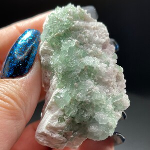 May include: A cluster of green apophyllite crystals on a white matrix. The crystals are translucent and have a glassy lustre.