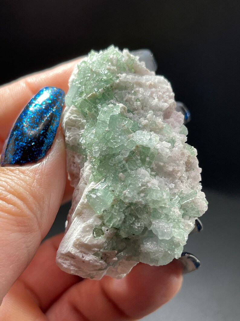 May include: A cluster of green apophyllite crystals on a white matrix. The crystals are translucent and have a glassy lustre.